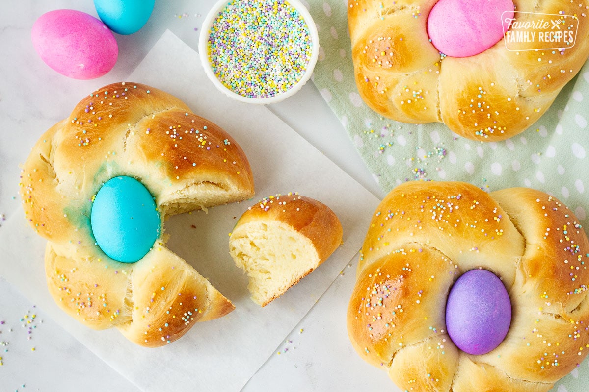Piece of Easter Bread next to Easter Bread loaf. Sprinkles and colored eggs on the side.