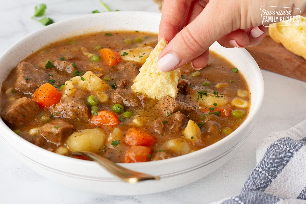 Hand dipping a piece of roll into a bowl of Hearty Beef Stew.