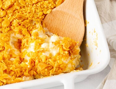 Wooden spoon scooping Cheesy Potato Casserole from a baking dish.