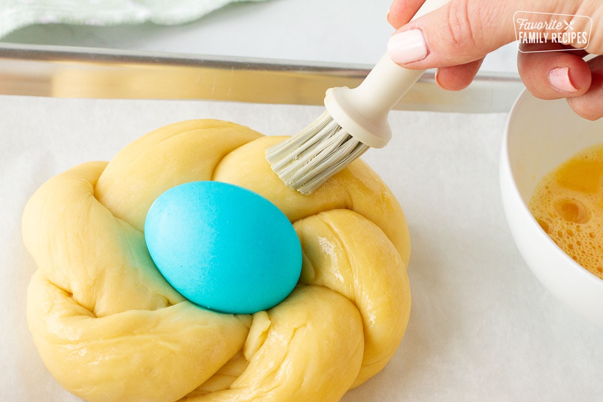 Brushing egg wash around the outside of the Easter Bread loaf. Blue colored egg in the center.