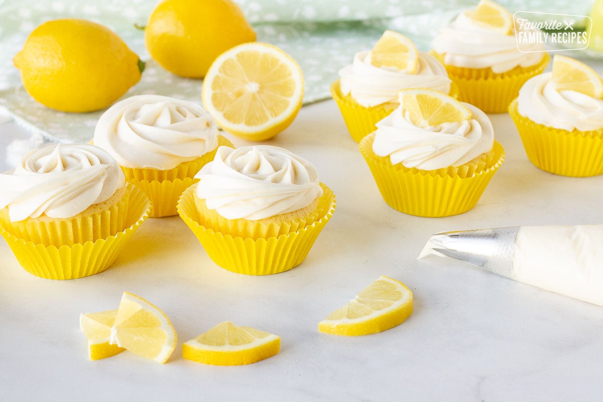 Frosting Lemon Cupcakes with a piping tip and lemon slices on the top and sides.