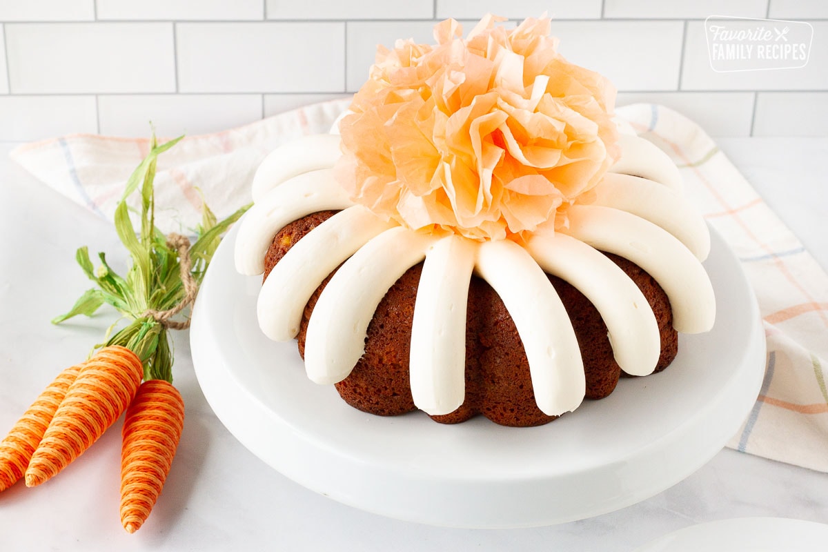 Carrot Bundt Cake on a cake stand with prop carrots on the side and a tissue pom pom in the center.