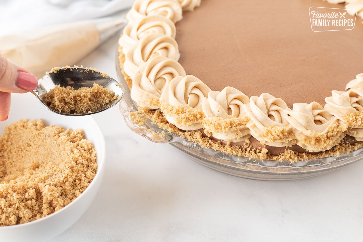 Sprinkling graham cracker crumble mixture on the sides of the Costco Peanut Butter Chocolate Cream Pie.