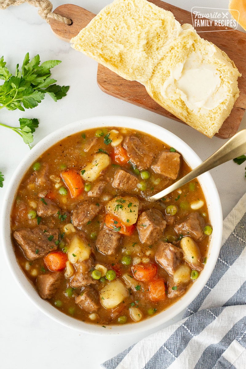 Bowl of Hearty Beef Stew with a spoon and a buttered dinner roll on the side.