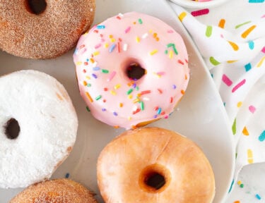 Top view of Homemade Donuts on a plate including glazed, cinnamon sugar, powdered sugar and pink frosting with sprinkles.