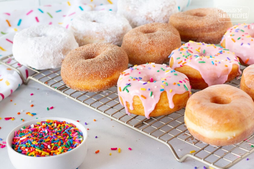 Decorated Homemade Donuts on a cooling rack with sprinkles on the side.