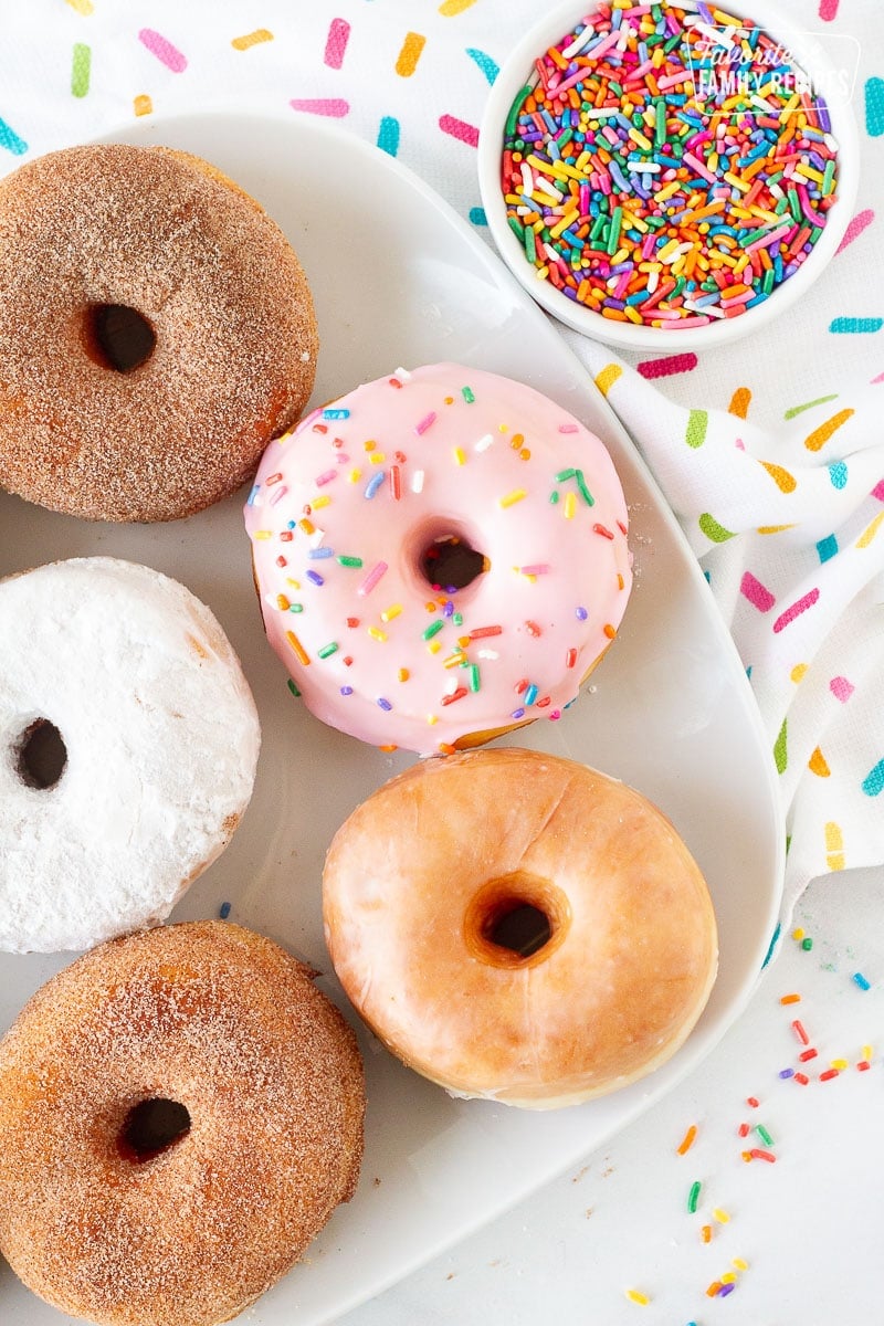 Top view of Homemade Donuts on a plate including glazed, cinnamon sugar, powdered sugar and pink frosting with sprinkles.