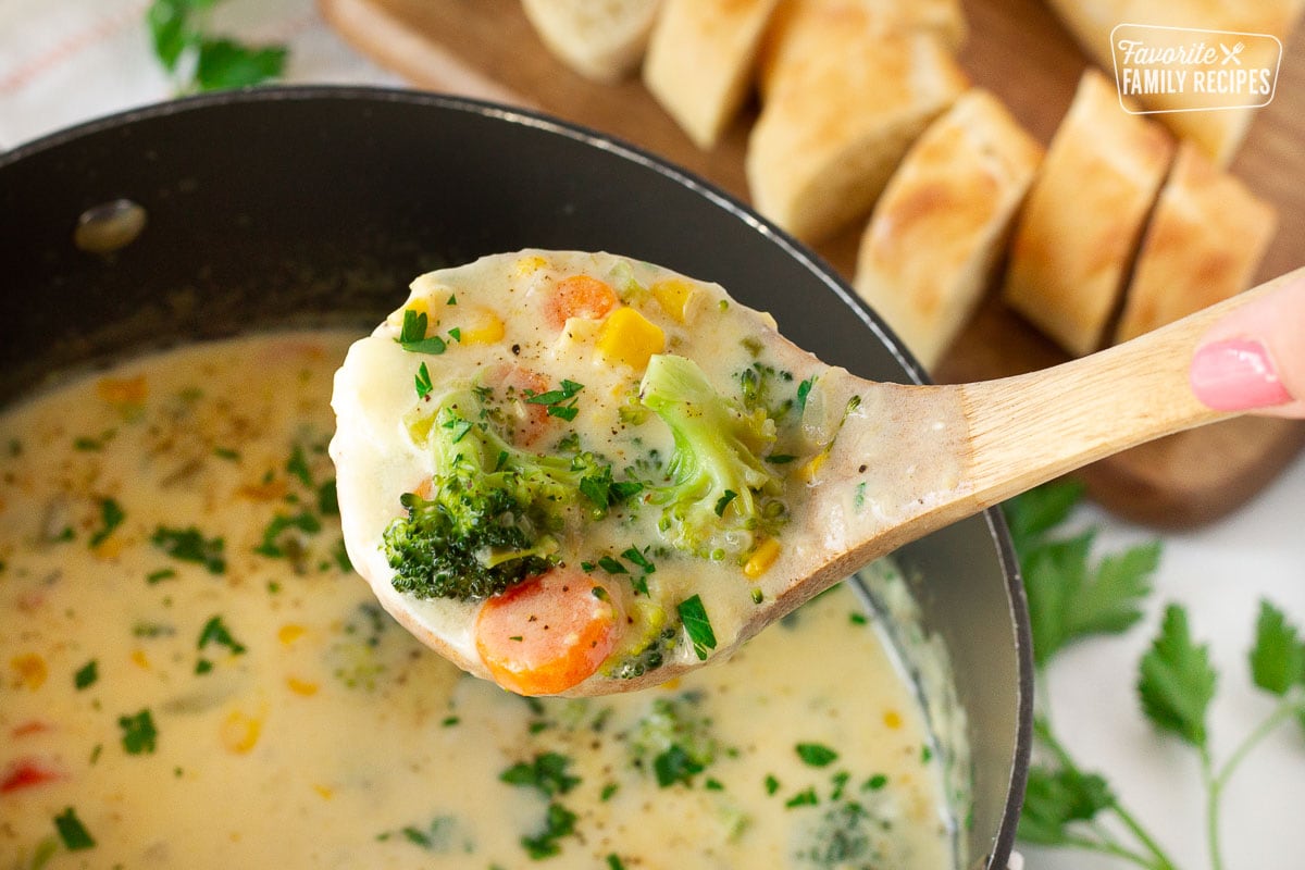 Ladle holding a scoop of Creamy Vegetable Soup with broccoli, corn, carrots and potato.