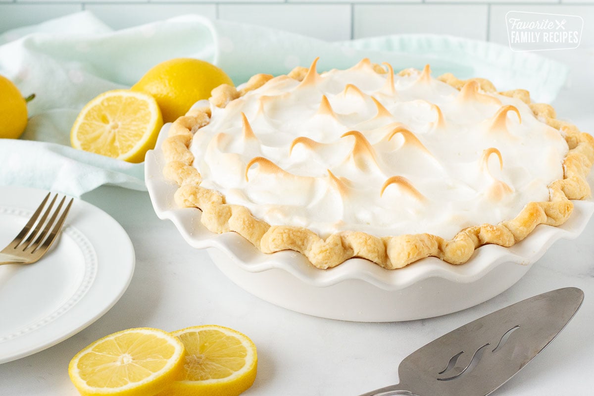 Whole Lemon Meringue Pie in a pie plate next to a plate with fork and serving spatula.