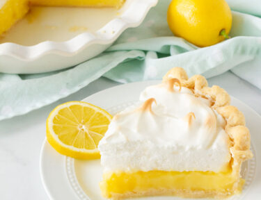 Slice of Lemon Meringue Pie on a plate with sliced lemons.
