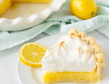 Slice of Lemon Meringue Pie on a plate with sliced lemons.