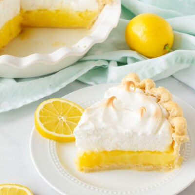 Slice of Lemon Meringue Pie on a plate with sliced lemons.
