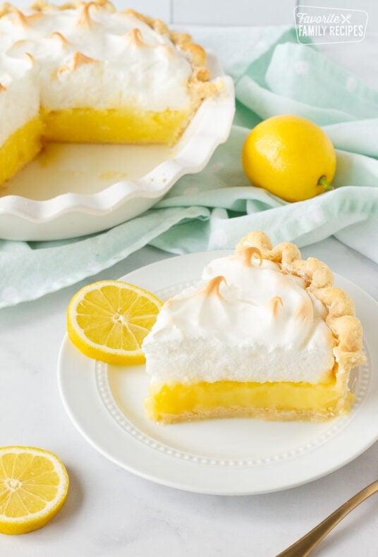 Slice of Lemon Meringue Pie on a plate with sliced lemons.