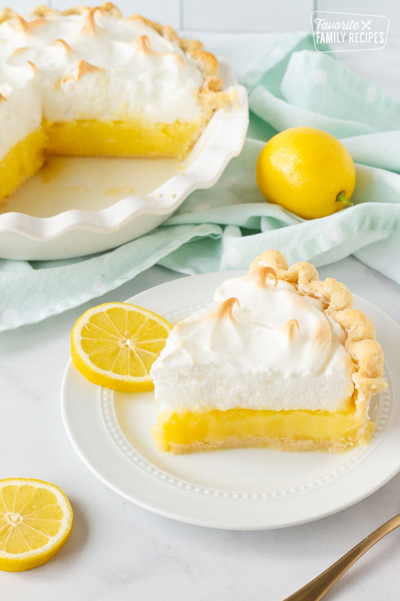 Slice of Lemon Meringue Pie on a plate with sliced lemons.