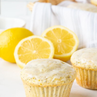 Close up off of a single Lemon Poppy Seed Muffin with one behind. Fresh lemons behind.