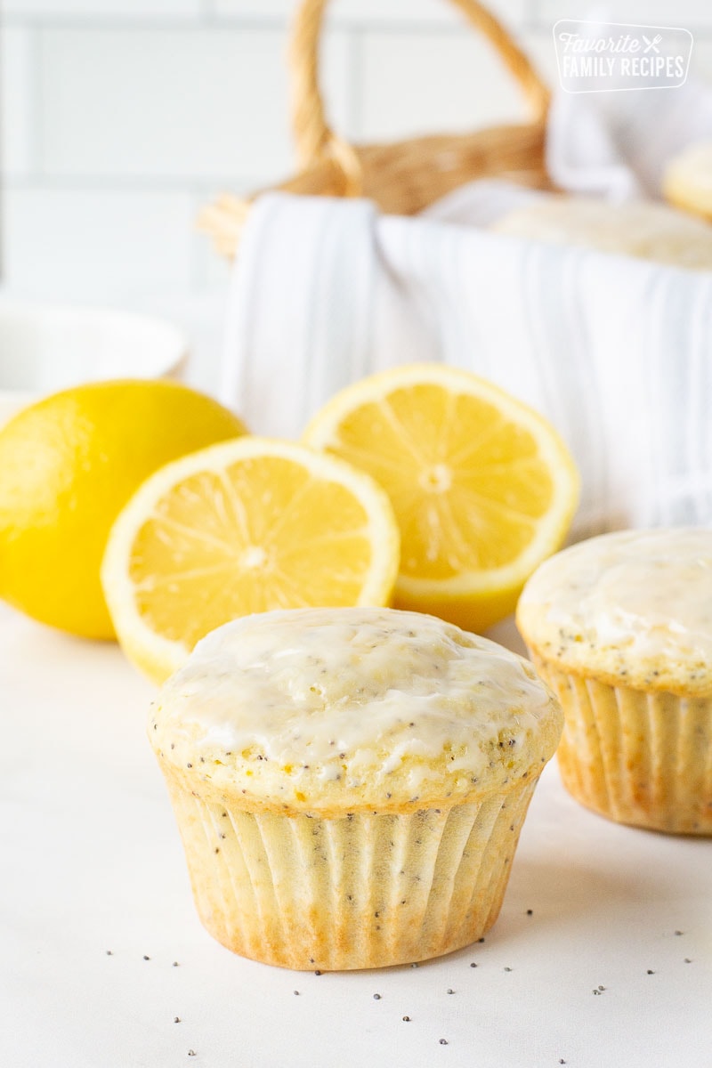 Close up off of a single Lemon Poppy Seed Muffin with one behind. Fresh lemons behind.