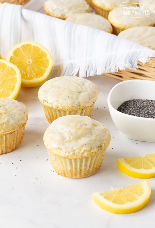 Three Lemon Poppy Seed Muffins in front of a basket of muffins.
