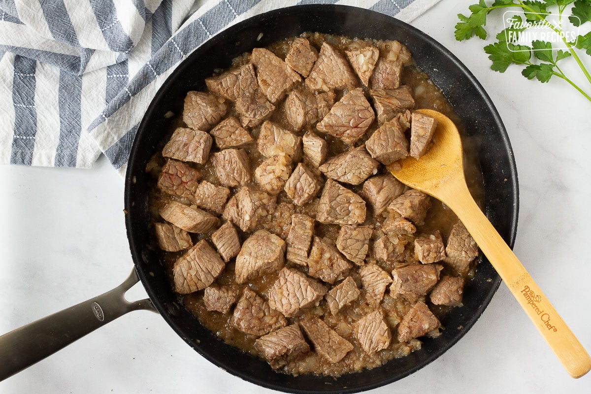 Skillet with Beef and onions with a wooden spoon for Hearty Beef Stew.