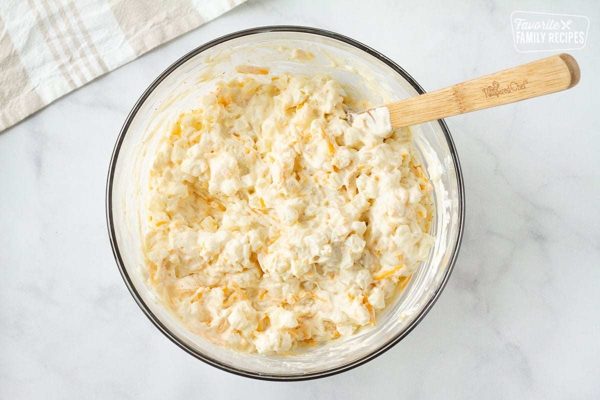 Bowl of Cheesy Potato Casserole mixture with a wooden spoon.