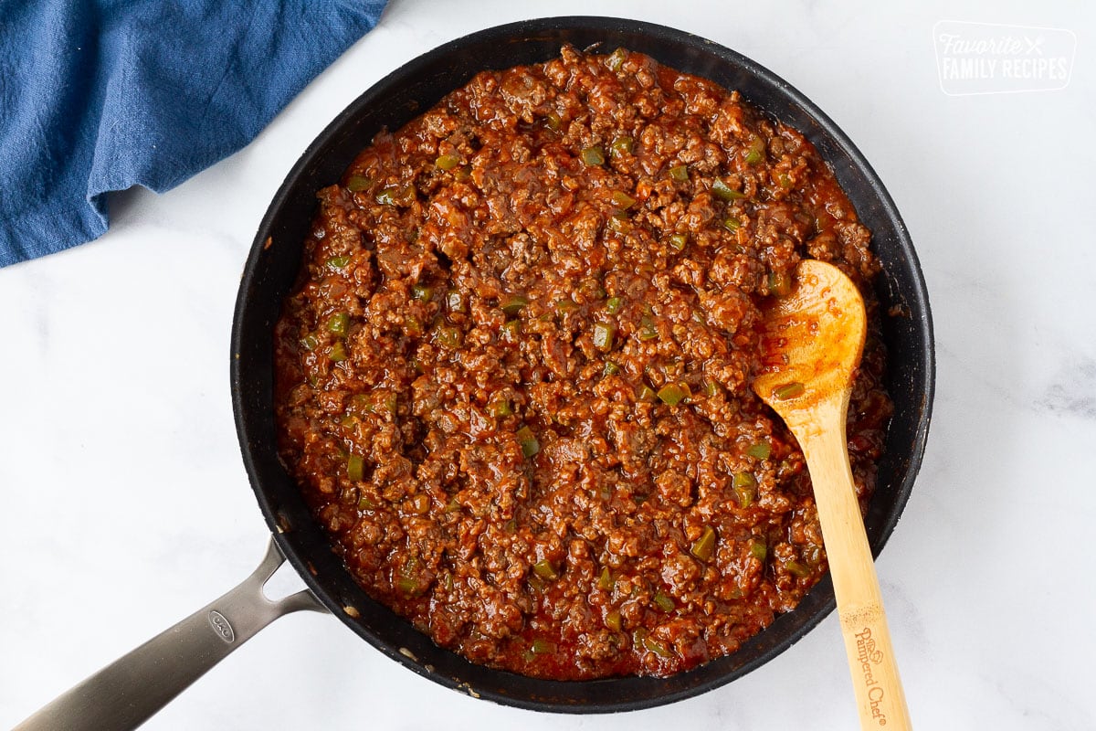 Skillet with wooden spoon of sauce, cooked ground beef, onion and green bell peppers for Homemade Sloppy Joes.