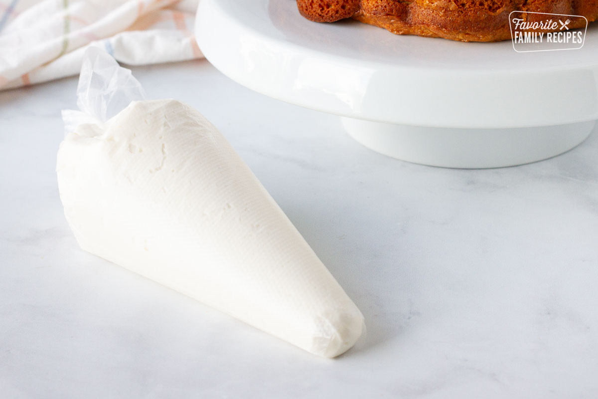Piping bag with cream cheese frosting and cut off tip with Carrot Bundt Cake in the background.