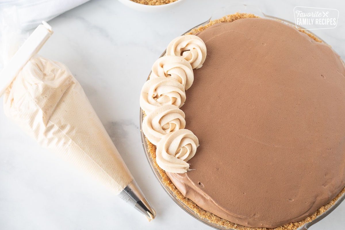 Piping the peanut butter border with a piping bag on a Costco Peanut Butter Chocolate Cream Pie.