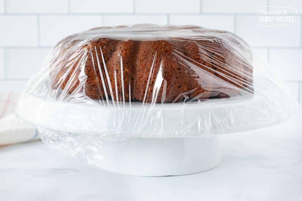 Carrot Bundt Cake wrapped in plastic wrap on a cake stand.