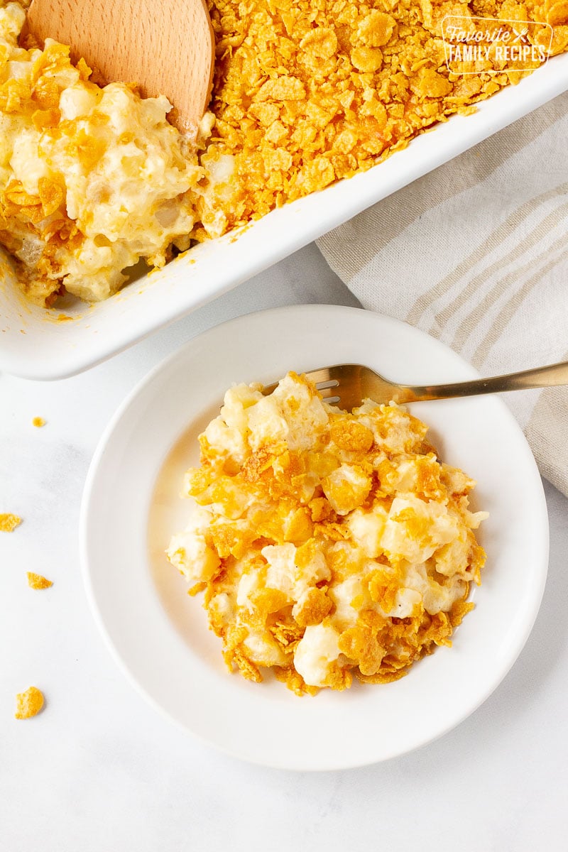 Plate of Cheesy Potato Casserole with a fork next to the baking dish of Cheesy Potato Casserole.