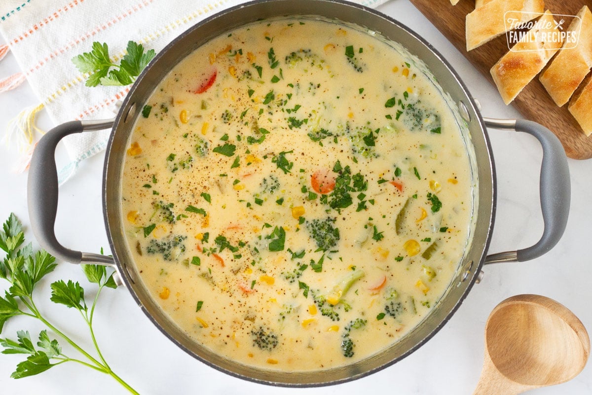 Large pot of Creamy Vegetable Soup with a ladle and a cutting board of sliced French bread.