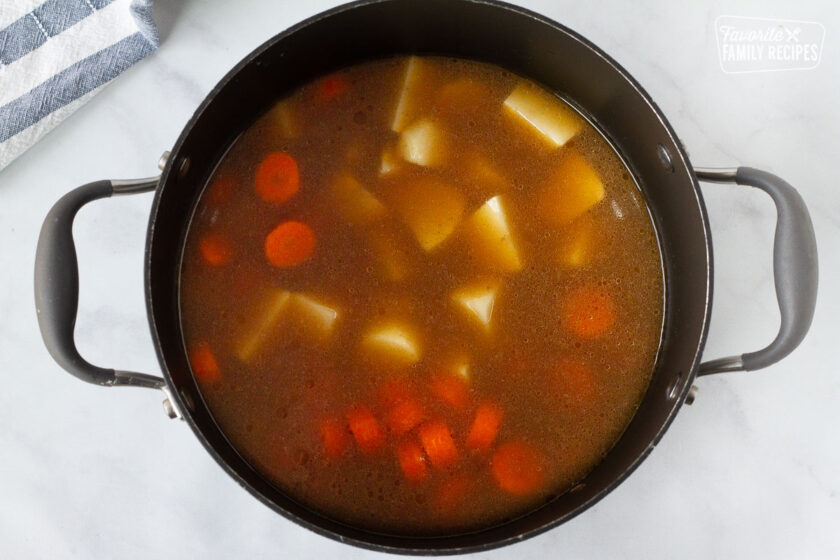Pot with beef cubes, beef broth, carrots and potatoes for Hearty Beef Stew.