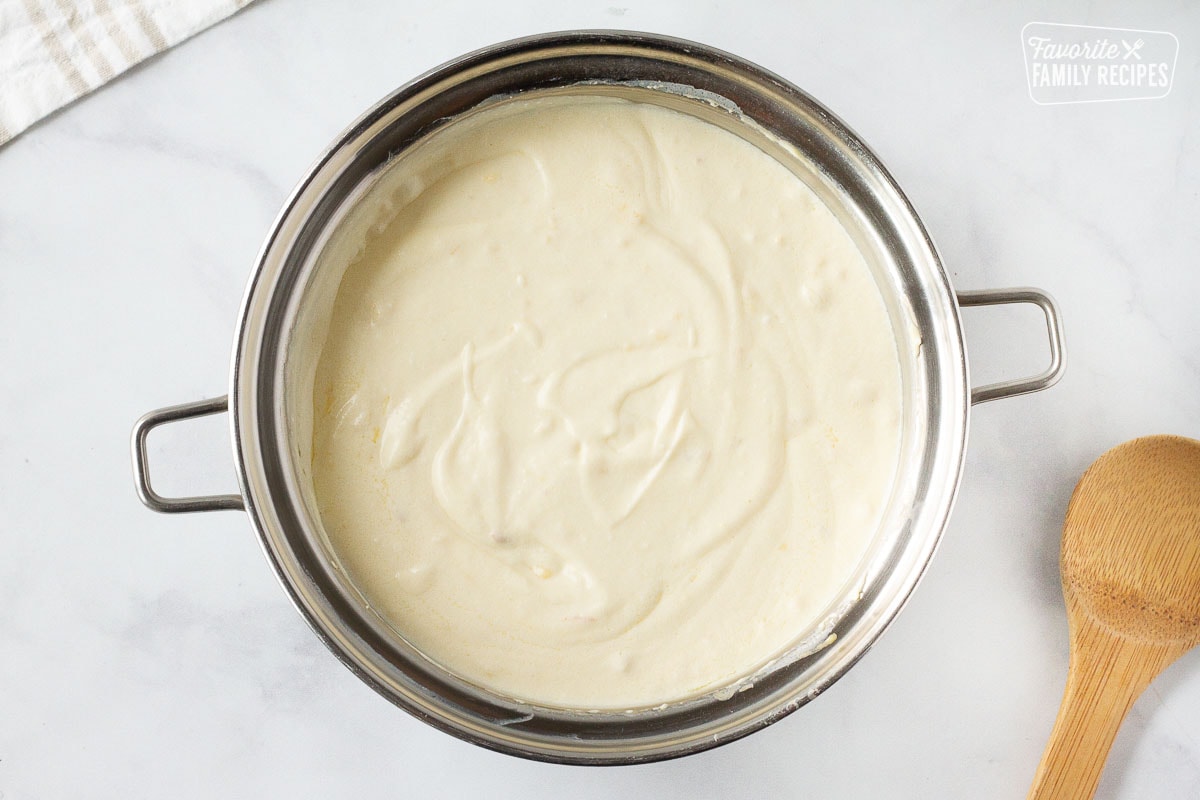 Sauce pan of creamy sauce for Cheesy Potato Casserole with a wooden spoon on the side.