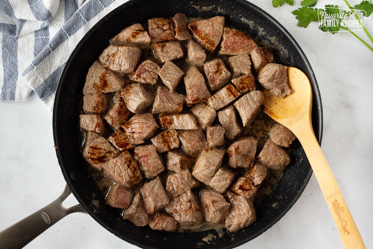 Wooden spoon stirring seasoned beef for Hearty Beef Stew.