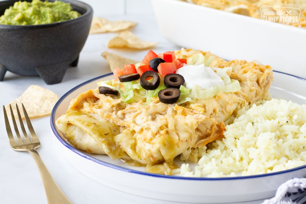Plate of Sour Cream Chicken Enchiladas topped with sour cream, olives, lettuce and tomatoes. Guacamole and chips on the side.