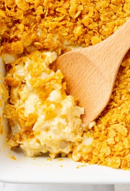 Cheesy Potato Casserole with crunchy topping in a baking dish with a wooden spoon for scooping.