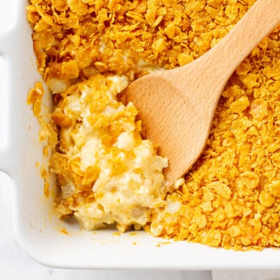 Cheesy Potato Casserole in a baking dish with a wooden spoon for scooping.