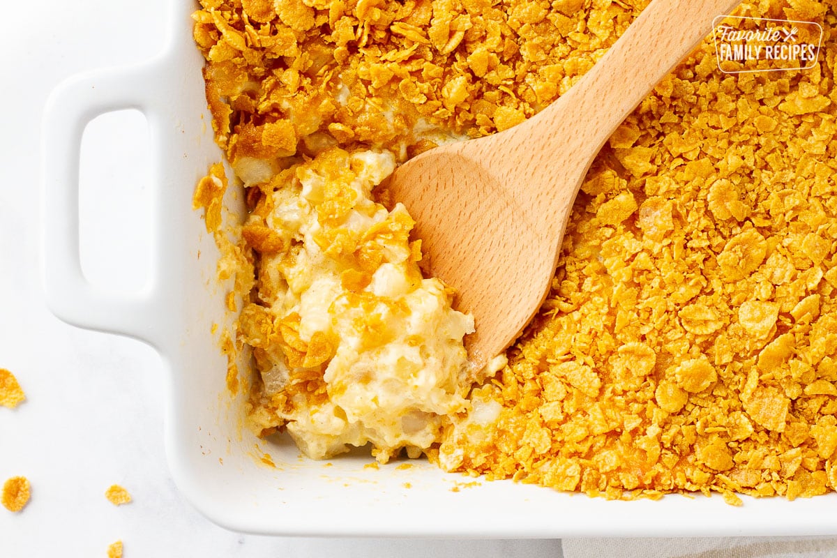 Cheesy Potato Casserole in a baking dish with a wooden spoon for scooping.