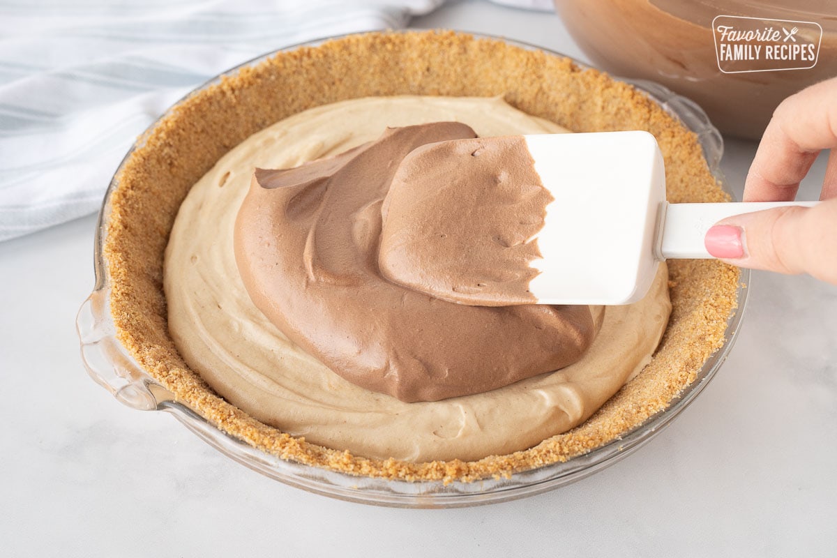 Spreading chocolate mousse layer on top of the peanut butter layer with a spatula on a Costco Peanut Butter Chocolate Cream Pie.