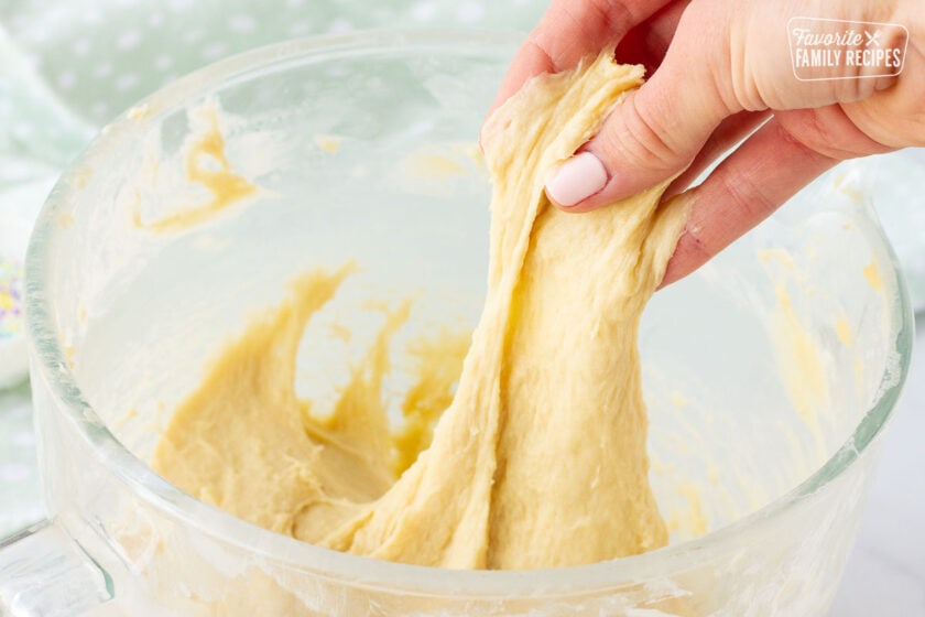 Hand stretching Easter Bread dough out of a mixing bowl.