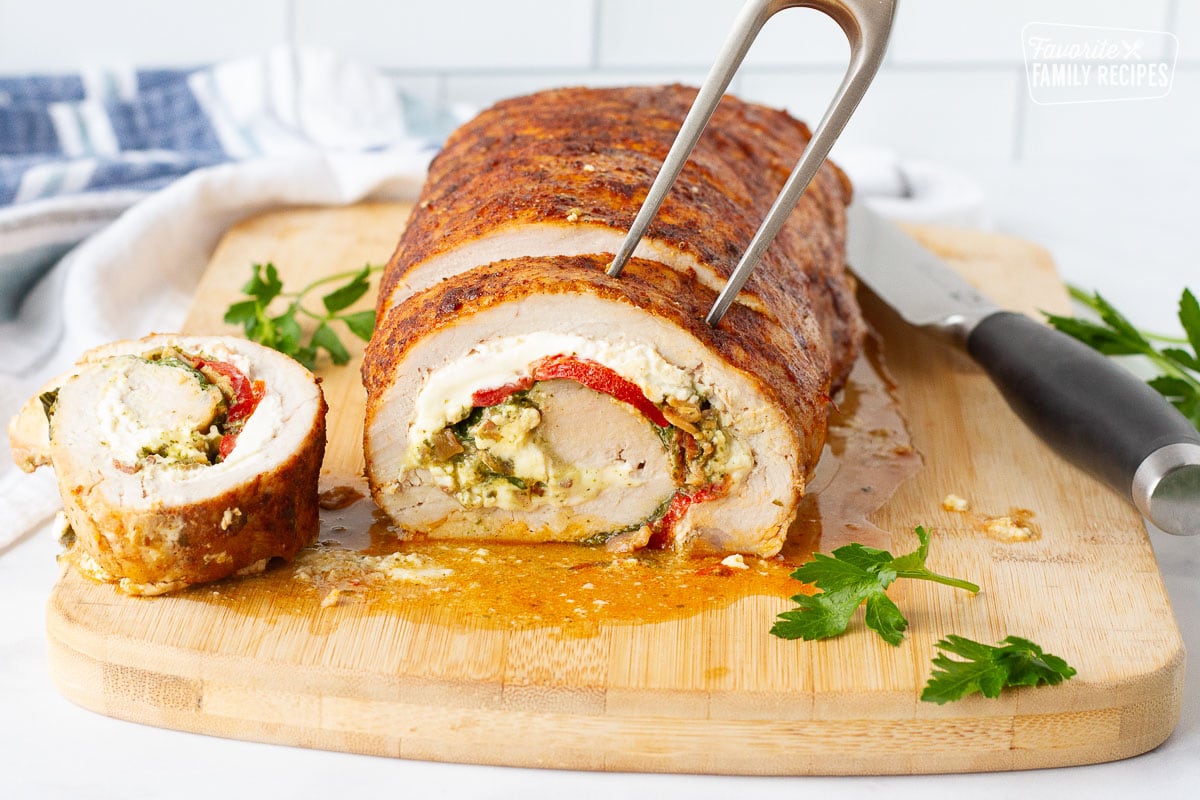 Stuffed Pork Loin on a cutting board with a fork into one piece.