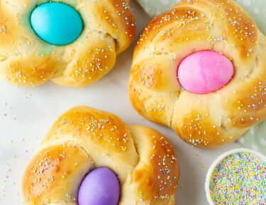 Three Easter Bread loaves with pink, blue and purple colored eggs in the center.