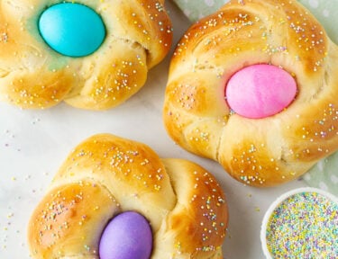 Three Easter Bread loaves with pink, blue and purple colored eggs in the center.