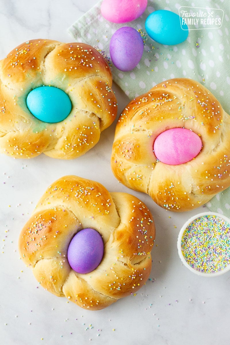 Three Easter Bread loaves with pink, blue and purple colored eggs in the center.
