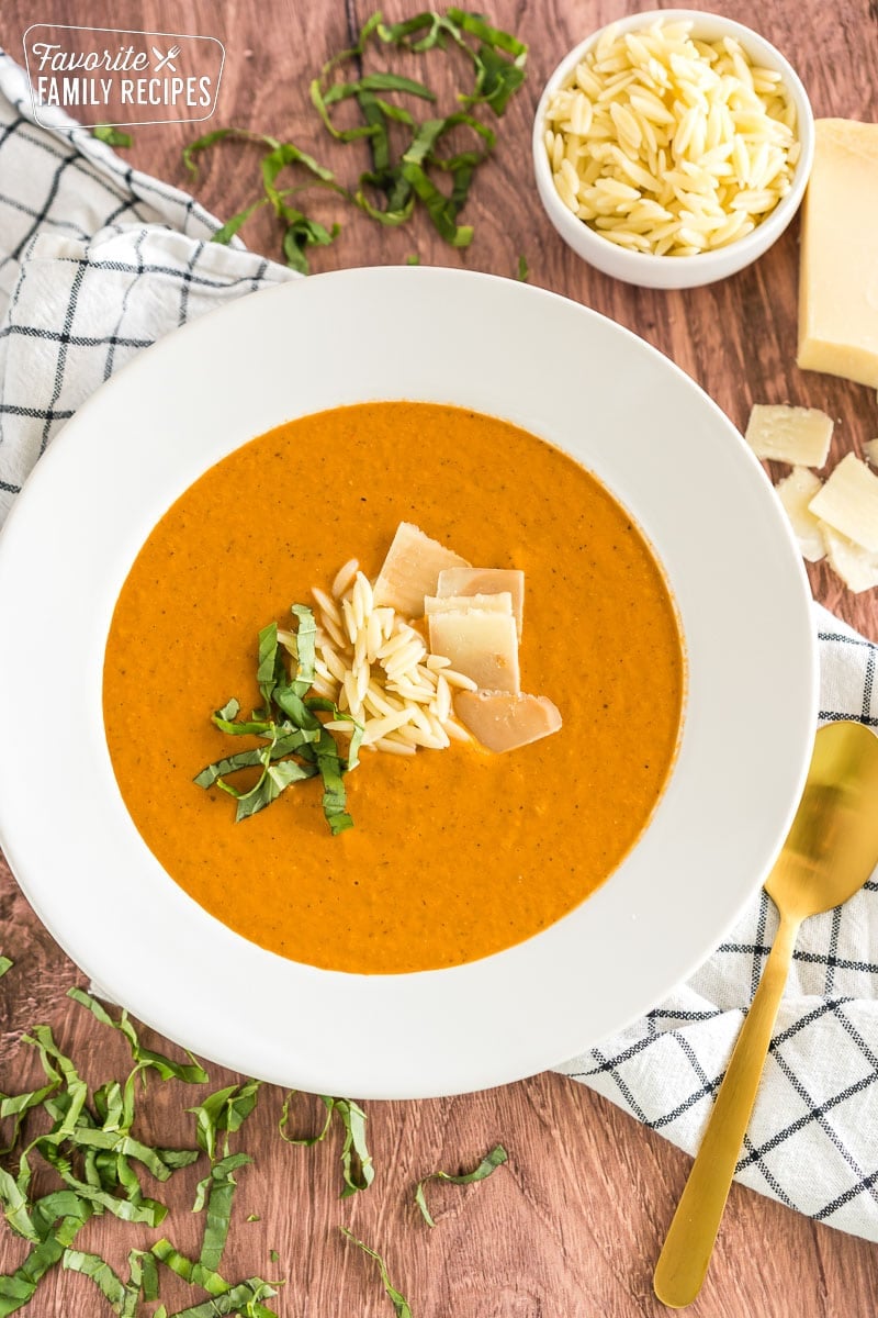 A bowl of tomato basil soup topped with orzo, parmesan cheese, and basil.