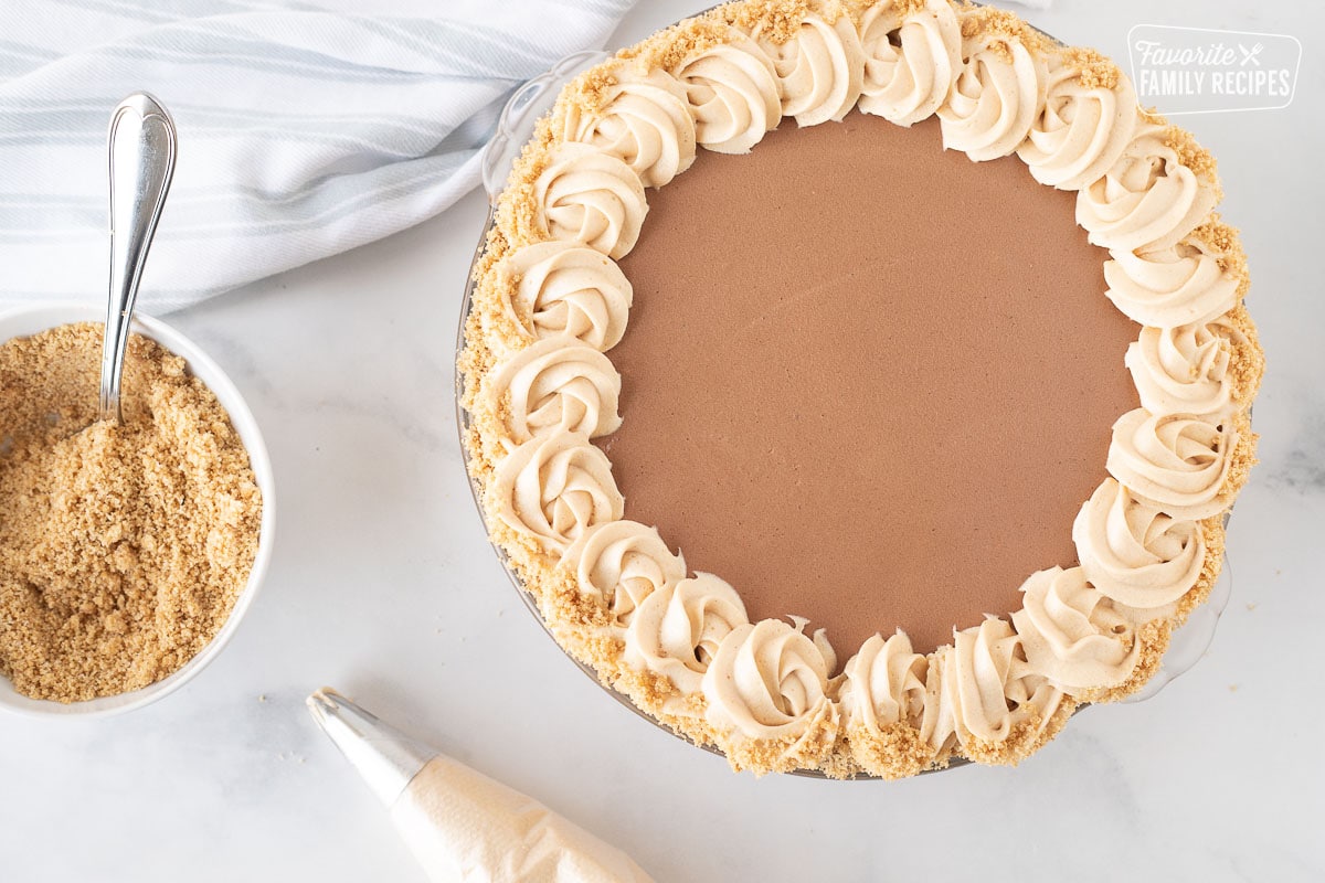 Top view of a Costco Peanut Butter Chocolate Cream Pie with a piping bag and bowl of graham cracker crumbs on the side.