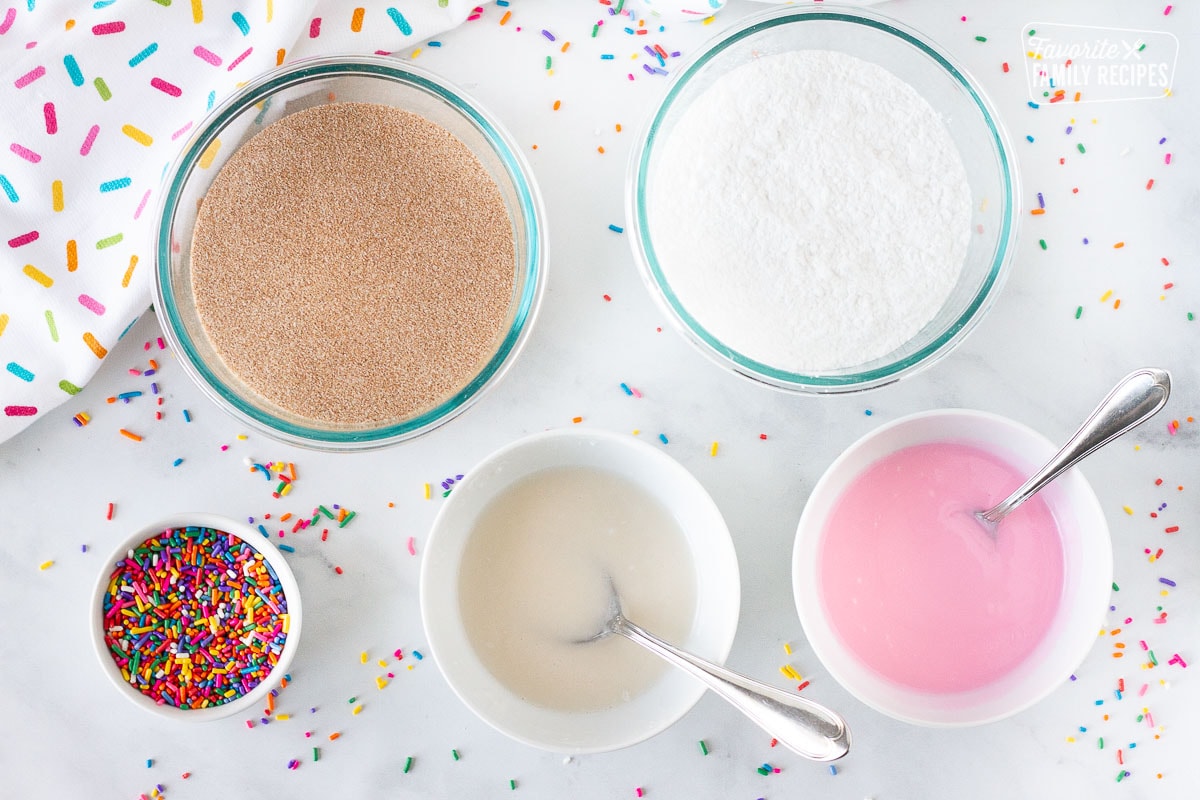 Toppings for Homemade Donuts including cinnamon sugar, powdered sugar, glaze, sprinkles and pink frosting.