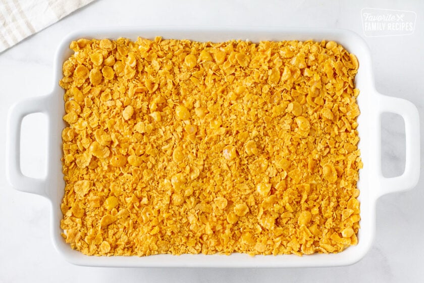 Cheesy Potato Casserole in a baking dish topped with crushed corn flakes and melted butter.