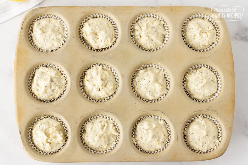 Muffin pan filled with lined unbaked Lemon Poppy Seed Muffins.