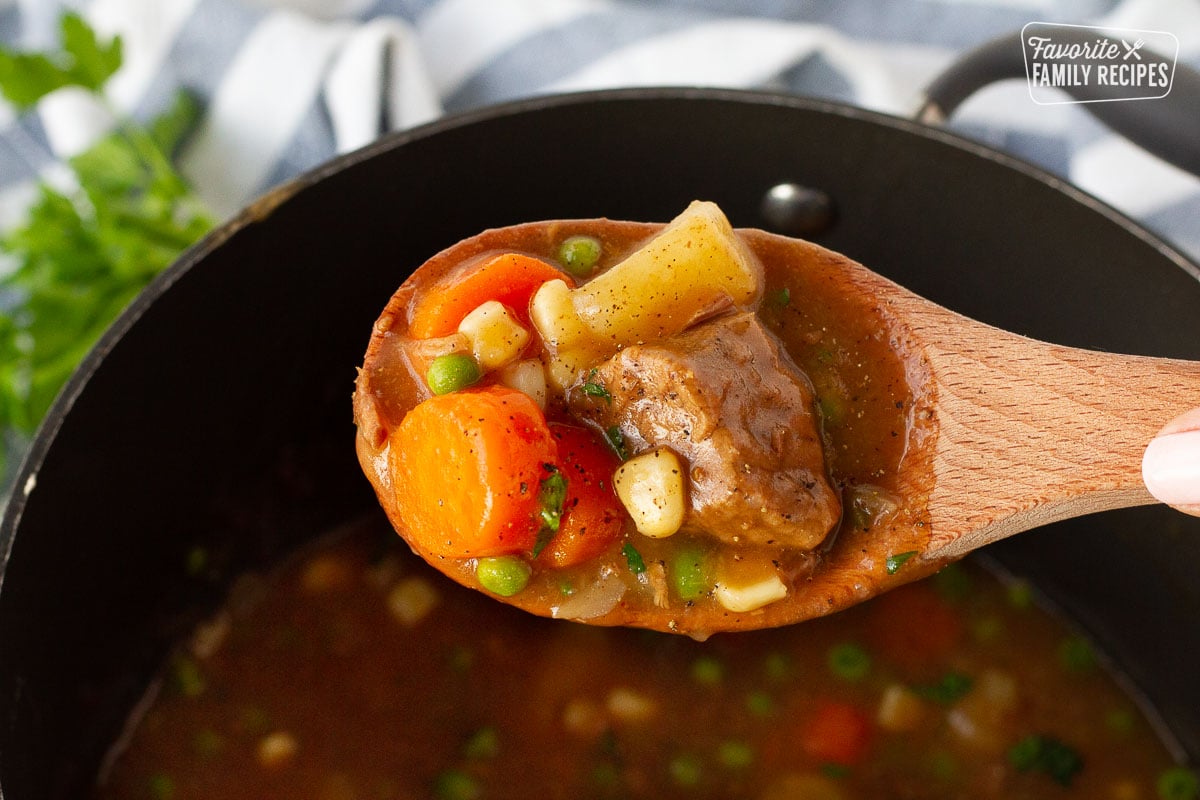 Wooden spoon holding a scoop of Hearty Beef Stew over the pot.