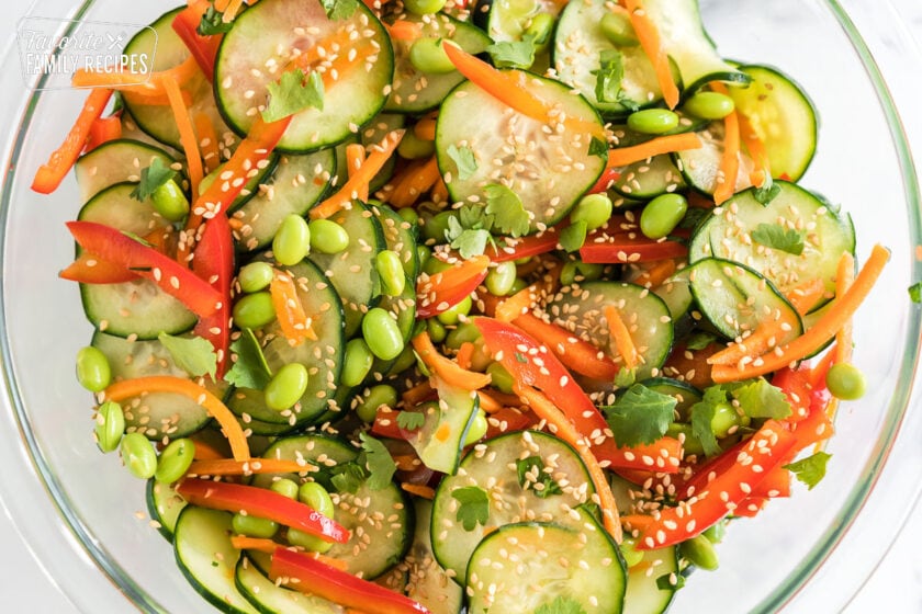 Asian cucumber salad in a large glass bowl topped with toasted sesame seeds and fresh cilantro