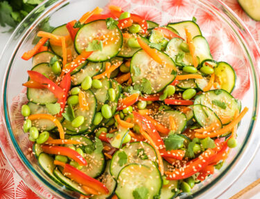 Asian cucumber salad in a large glass bowl topped with toasted sesame seeds and fresh cilantro